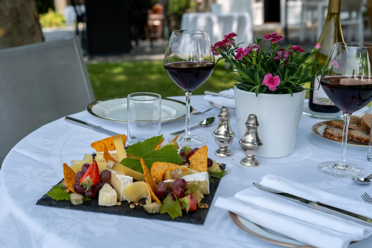 Table set in the garden for dinner: Beaujolais wine glasses, cheese board and a carefully laid place setting
